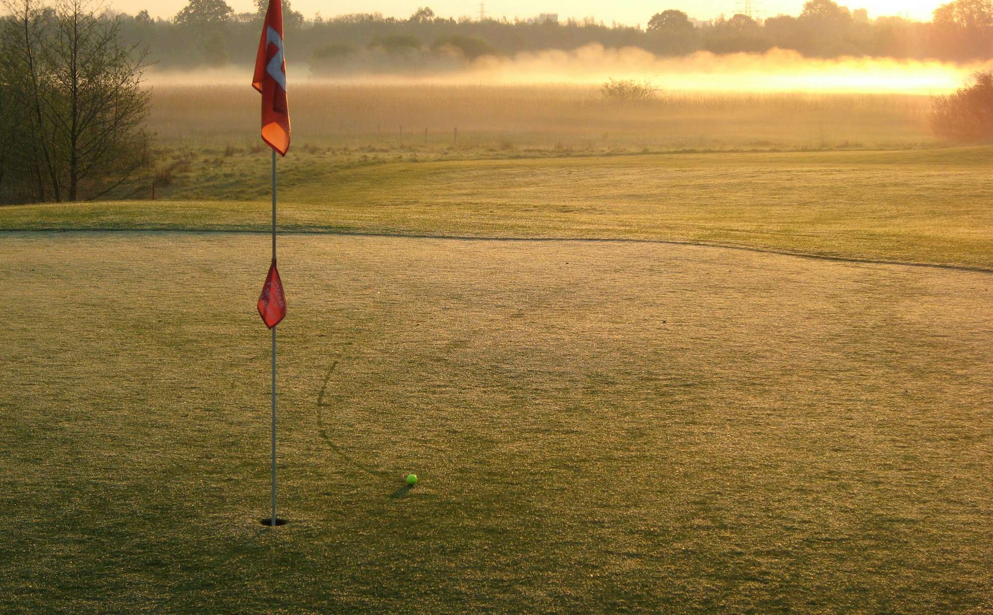 Red flag on a golf green at dawn